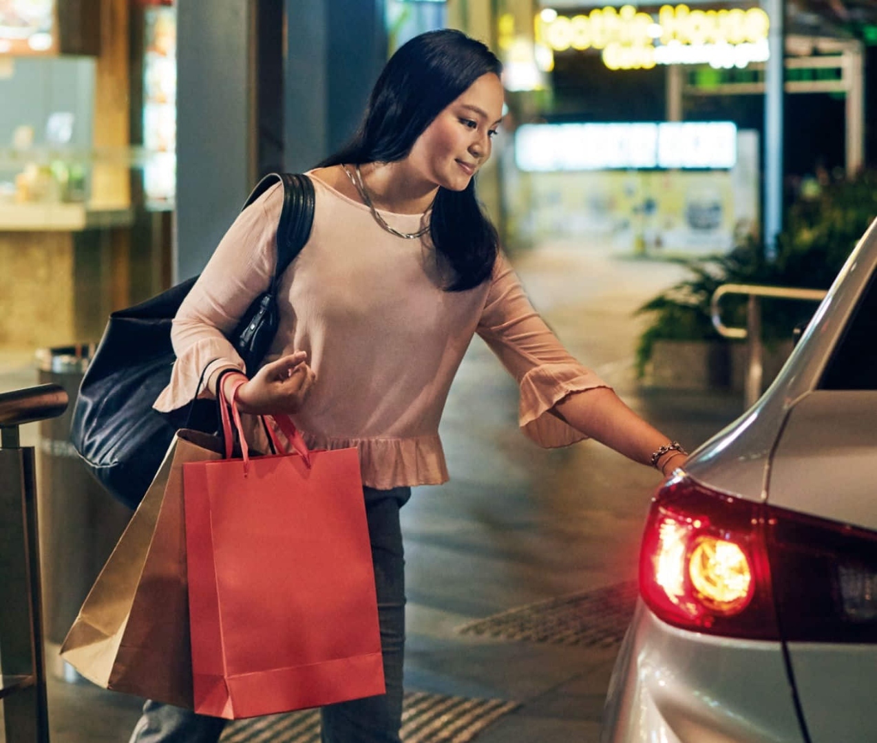 Woman with shopping bags getting into her ride outside a shopping centre at night